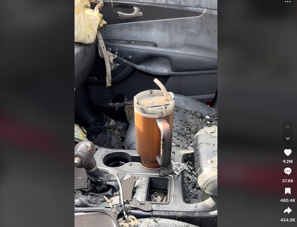 An image of a burnt out automobile with a pristine Stanley travel mug sitting in the cup holder.