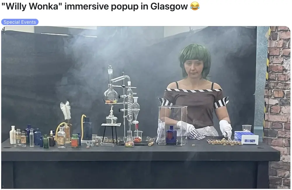 A woman in costume stands behind a table with lab equipment and bottles at a smoky Willy Wonka-themed popup event.
